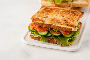 Sandwich with salmon, fresh salad and cucumber on a white board. Copy space.