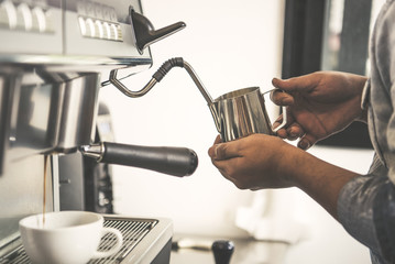 Barista using coffeemaker extraction for espresso shot and steam milk in cafe.