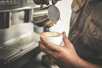 Barista making latte or Cappuccino art with frothy foam, coffee cup in cafe.