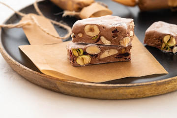 A variety of different nutty nougat in dark chocolate with roasted hazelnuts cut open to show the nougat mix on a wooden board . Copy space.