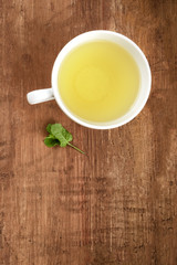 A photo of a cup of green tea tea with a mint leaf, shot from the top on a dark rustic wooden background with a place for text