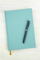 A photo of a teal blue journal with a pen, an elegant notebook or planner with copy space, shot from the top