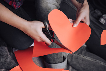 woman cuts red paper heart by scissors on Valentine's Day on the bed. Close-up