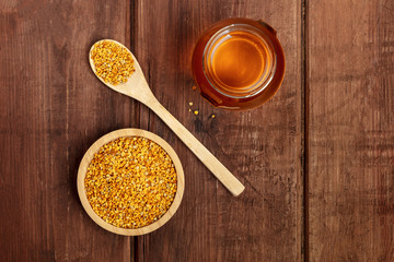 Healthy organic food. Bee pollen, a jar of honey, and a wooden spoon, shot from the top on a dark wooden background with copy space