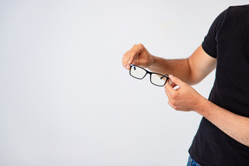 fashionable glasses with a black frame are in the hands of a man on a white background in the studio. Adult man is dressed in black t-shirt. Close-up