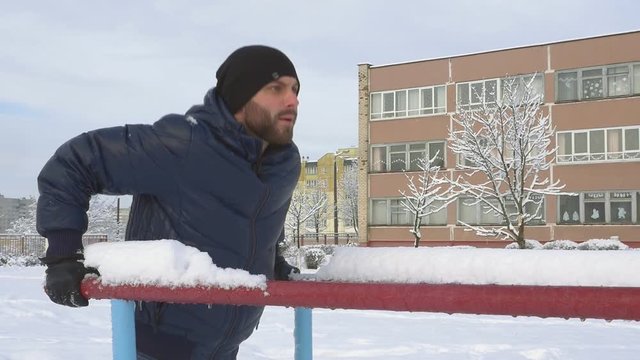 Young man doing triceps dip on parallel bars outdoors in winter slow motion
