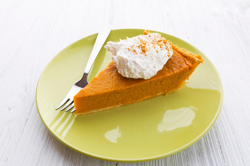 Slice of pumpkin pie with whipped cream over white wooden background