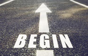 new start, road surface marking and traffic concept - close up of arrow and word begin on asphalt