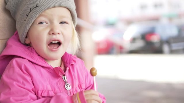 girl with candy on a stick. Baby laughs, stands at the store with a chupa chups in their hands. Vanilla candy is a favorite treat for a girl. She eats her