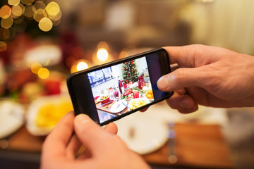 technology, eating and holidays concept - close up of male hands photographing food by smartphone at christmas dinner