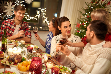 holidays and celebration concept - happy friends having christmas dinner at home, drinking red wine and clinking glasses