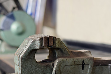 Vise close up on metal workshop. Bench grinder on background. Copy space.