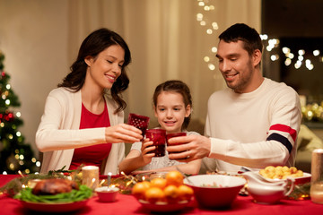 holidays, family and celebration concept - happy mother, father and little daughter with drinks toasting at home christmas dinner