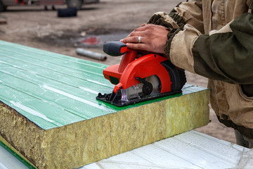 A young man builder in a working overall  grinds a sandwich panels  with a angle  grinder in the...