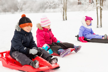 childhood, sledging and season concept - group of happy little kids sliding on sleds in winter
