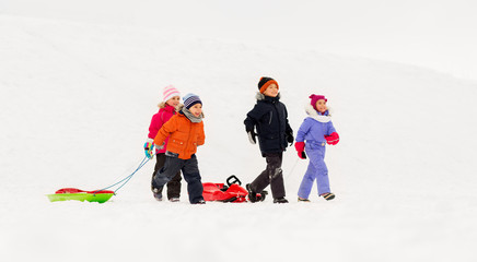 childhood, sledging and season concept - group of happy little kids with sleds in winter