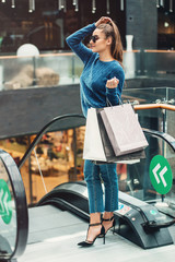 Beautiful girl with paper bags on escalator at supermarket