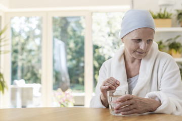 Senior woman suffering from ovarian cancer wearing bathrobe and headscarf taking pills at home.