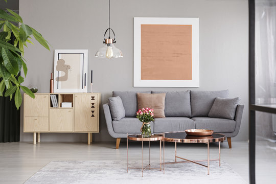 Large painting on a gray wall above an elegant sofa with cushions in a stylish living room interior with copper furniture