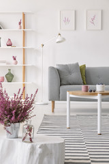 Heater in pot on the small wooden table in elegant scandinavian living room with grey couch and white lamp, real photo
