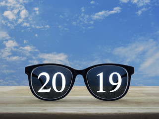 2019 white text with black eye glasses on wooden table over blue sky with white clouds, Business vision happy new year 2019 concept