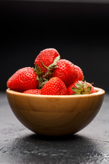 Photo of ripe strawberry in wooden cup on black background