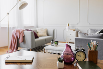 Table with notebook, small plant in pot, glass vase, clock and pencils in cup, real photo with copy space