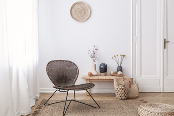Dark, modern wicker chair in a white living room interior with a wooden bench and decorations made...