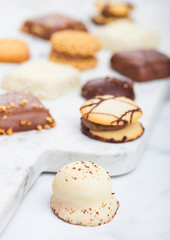 Luxury belgian chocolate and biscuit cookies selection on marble board and white kitchen table background.