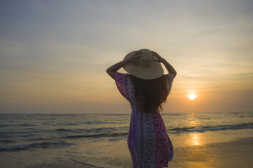 young happy and relaxed woman in Summer hat looking at the sun over the sea during an amazing beautiful sunset at tropical paradise beach in holidays travel
