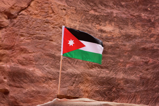 The flag of Jordan, shooting in the ancient stone city Petra, on the red rock background, close-up, outdoors. Copy space.