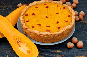 Autumn tart with goji berry decorated with hazelnuts on the black rustic wooden background. Traditional dessert for Thanksgiving holiday - pumpkin pie. Close up view