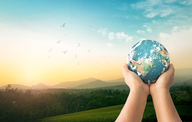 Earth Day concept: Human hands holding earth global over mountain sunrise background. Elements of this image furnished by NASA - obrazy, fototapety, plakaty