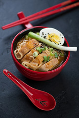 Red tableware with chicken ramen noodles, vertical shot over black stone background, selective focus