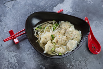 Bowl of wonton noodle soup on a grey concrete background, high angle view, studio shot