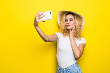 Portrait of girl having video-call with lover holding smart phone in hand shooting selfie on front camera isolated on yellow background. Enjoying weekend vacation