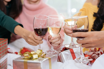 Hands of people celebrating New year party in home with wine drinking glasses and present background. New year and Christmas party concept. Happiness and Friendship and Funny together. Clinking glass