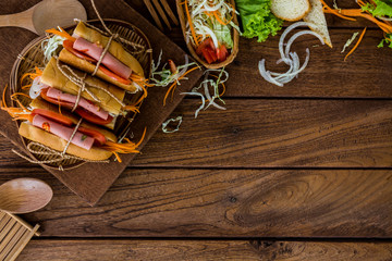 A delicious bologna peppers sandwiches with fresh vegetables on kitchen table and wooden board.