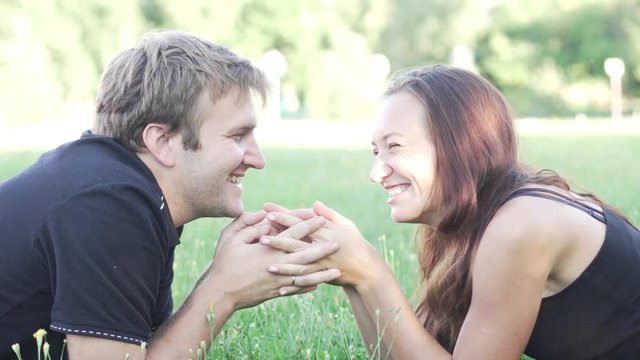 man and woman are lying on the green grass. They look at each other, hold hands, talk, laugh and kiss