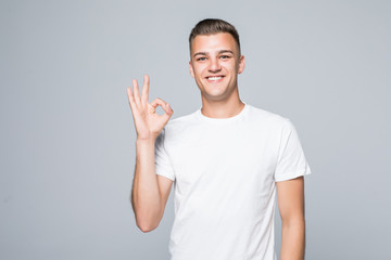 Fototapeta premium Portret wesoły młodzieniec Wyświetlono dobry gest na szarym tle