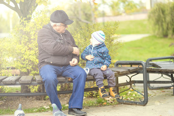 Fototapeta premium old grandfather and little grandson are sitting on a bench. concept of generations family. walk together