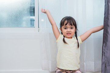 Fototapeta na wymiar Nice pretty child girl enjoys good sunny morning at home. Child girl wakes up from sleep. Girls stretching arms and raise hands. People health and baby lifestyles concept.
