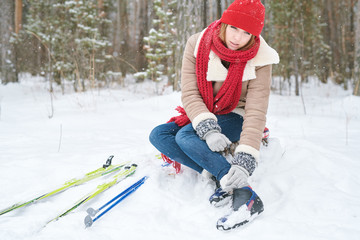 Full length portrait of beautiful young woman rubbing ankles after injury during ski walk in winter forest, copy space