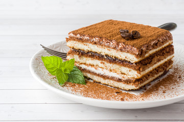 Delicious Tiramisu cake with coffee beans and fresh mint on a plate on a light background