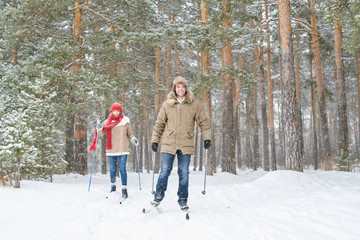 Full length portrait of modern active couple enjoying skiing in snowy winter forest during date, copy space