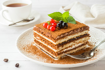 Delicious Tiramisu cake with fresh berries and mint on a plate on a light background. Breakfast with a Cup of coffee.