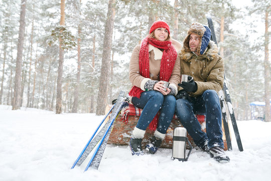 Full length portrait of active young couple  enjoying hot cocoa during ski date in beautiful winter forest, copy space