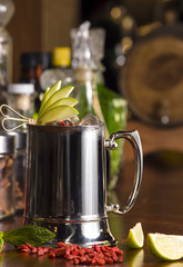 Stainless steel mug of tiki style beer cocktail with green apple goji berries. Mixed drink in a bar...