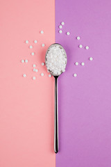 Sugar-replacing tablets with a spoon on a pink and purple background