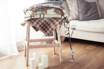 Fototapeta na wymiar Plaids. Autumn cozy interior. On a wooden chair is a stack of warm blankets. Candles. Autumn. Winter.